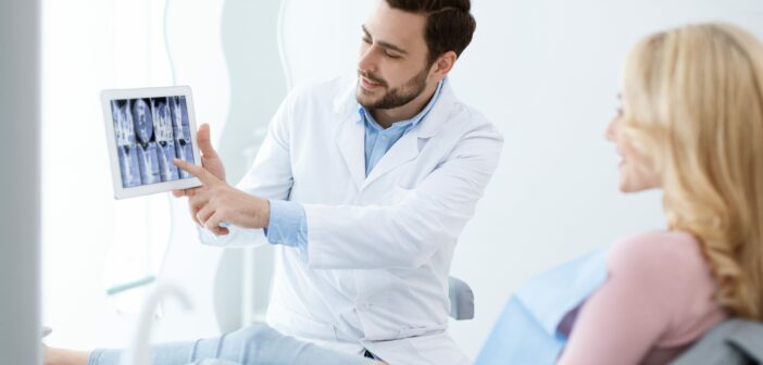 Zahnarzt zeigt Patienten mit einem Tablet Röntgenaufnahmen im Behandlungsraum