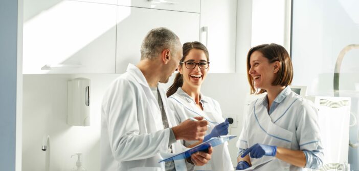Zwei Zahnärztinnen und ein Zahnarzt stehen im Behandlungszimmer und lachen miteinandner