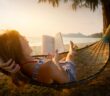 Frau liegt am Strand in der Hängematte und liest im Sonnenuntergang