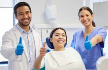 Ein Zahnarzt, eine Zahnarzthelferin und eine Patientin grinsen in die Kamera und halten den Daumen hoch.
