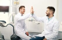 Zwei Zahnärzte klatschen sich im Behandlungsraum gegenseitig ab und lachen sich an